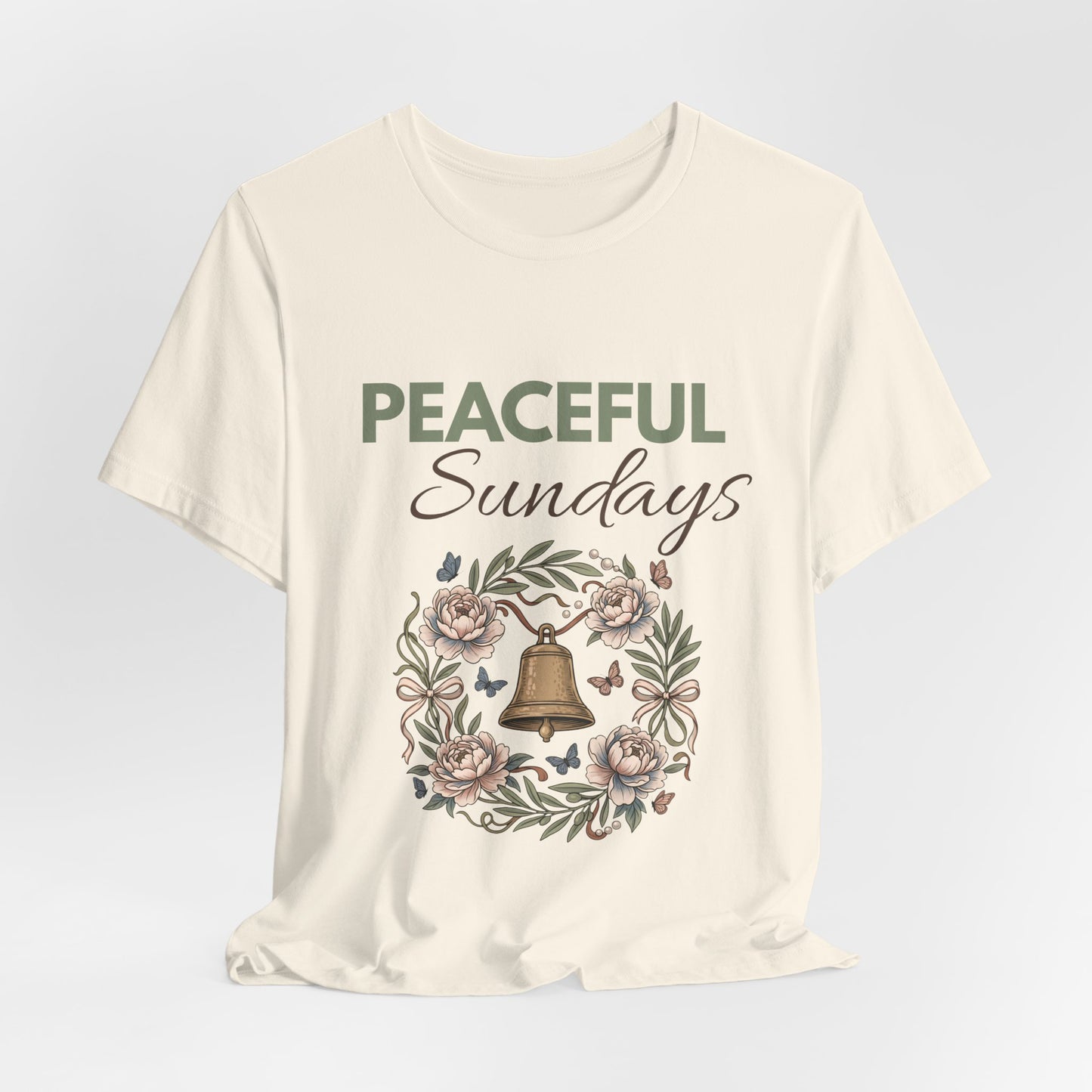 A natural colored t-shirt with 'Peaceful Sundays' design featuring a bell and flowers on a light gray background