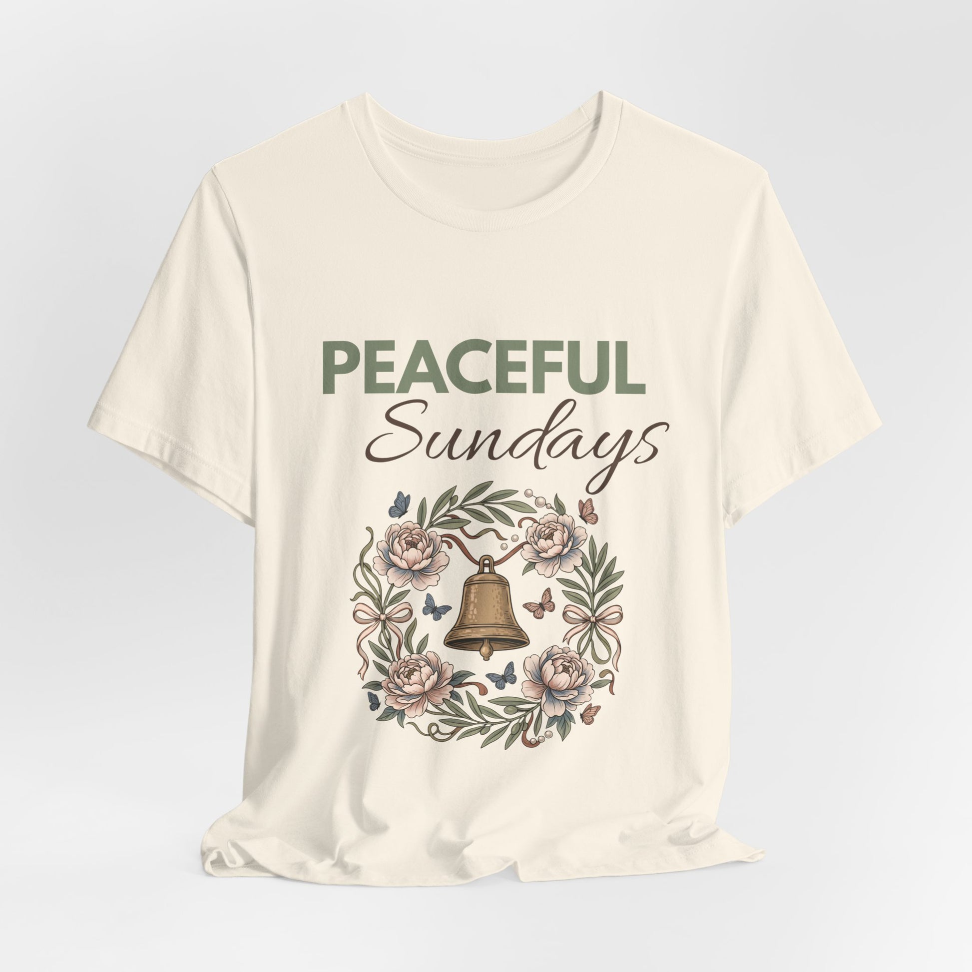 A natural colored t-shirt with 'Peaceful Sundays' design featuring a bell and flowers on a light gray background