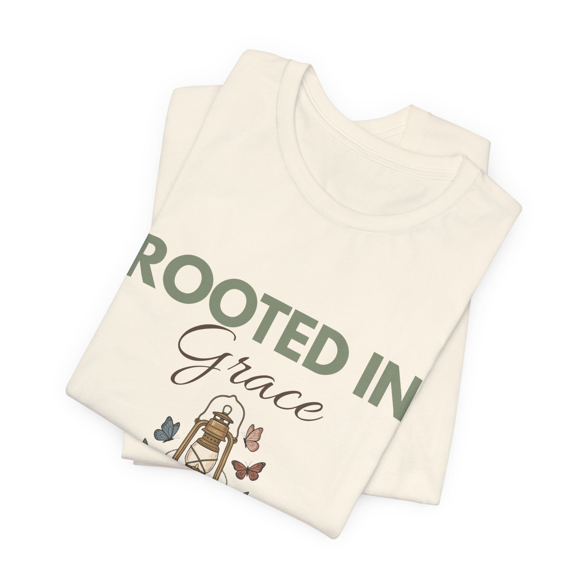 Folded natural colored t-shirt with 'Rooted in Grace' text and illustrations on a white background