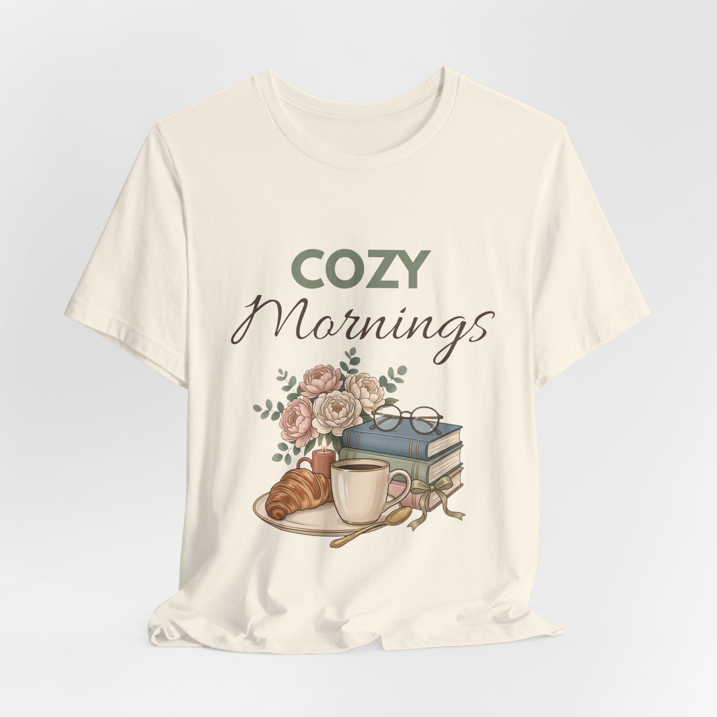 Natural colored t-shirt with 'Cozy Mornings' graphic design featuring a coffee cup, croissant, and books on a light gray background.