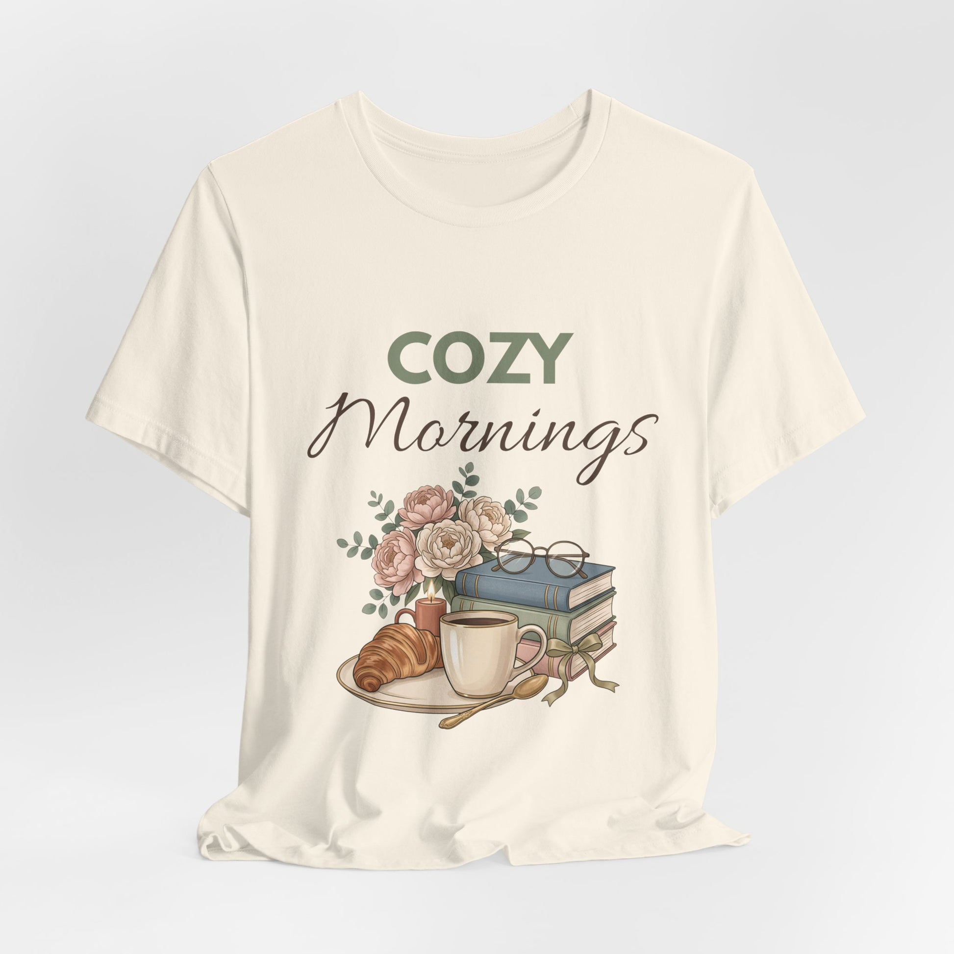 Natural colored t-shirt with 'Cozy Mornings' graphic design featuring a coffee cup, croissant, and books on a light gray background.