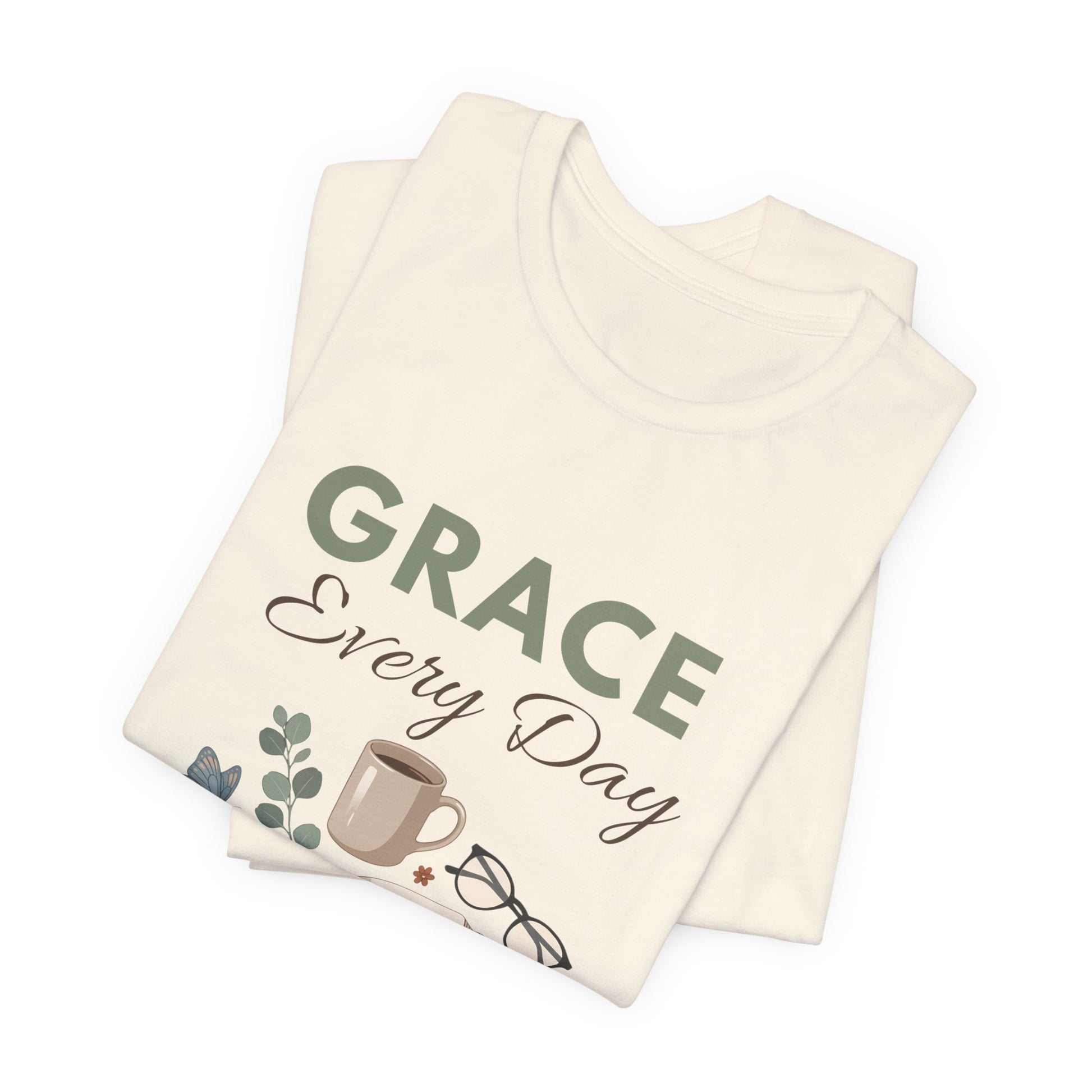 Folded natural colored t-shirt with 'GRACE Every Day' text and graphics on a white background