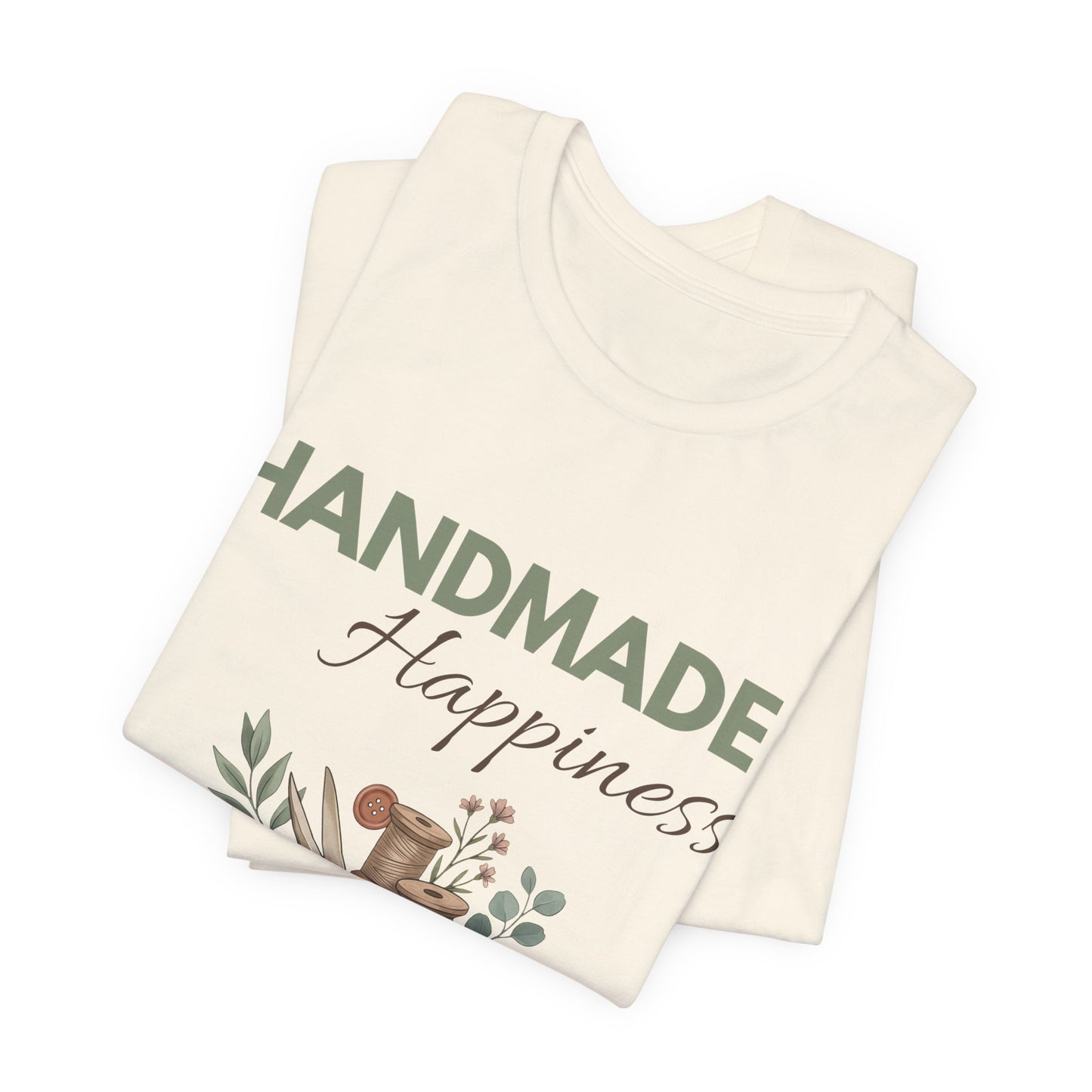 A folded natural colored t-shirt with 'HANDMADE Happiness' on the front.