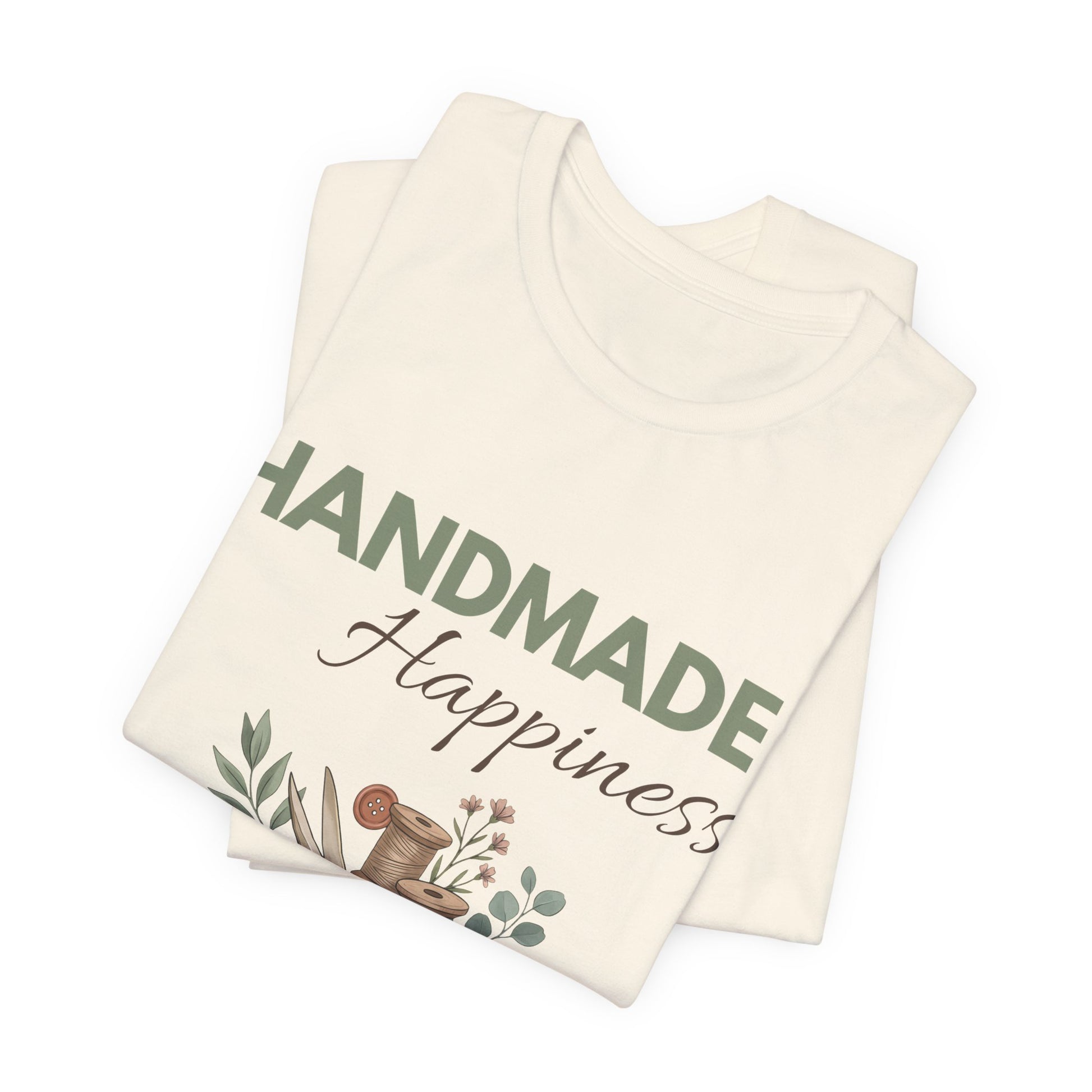 A folded natural colored t-shirt with 'HANDMADE Happiness' on the front.
