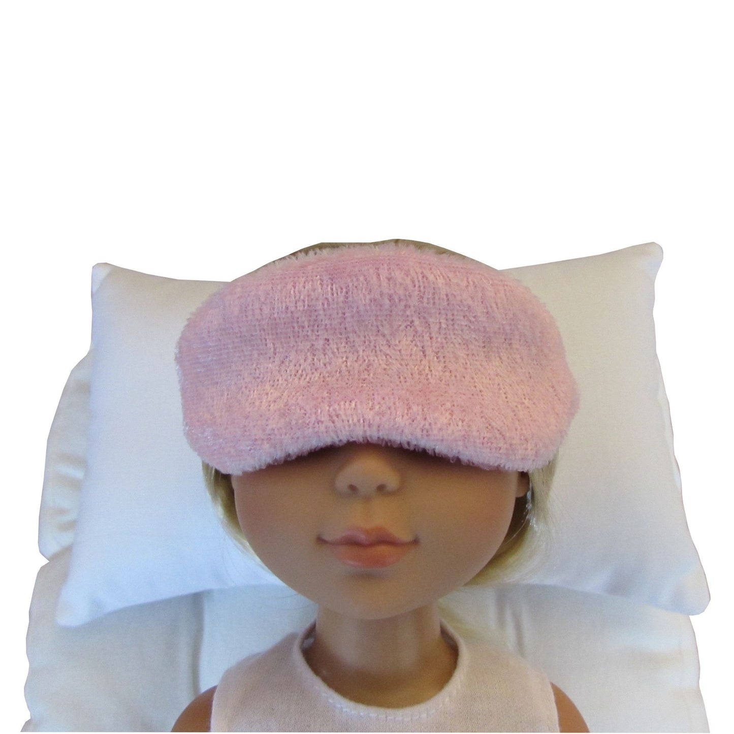 A pink panne velvet sleep mask worn by a doll, shown against a white pillow and white background.