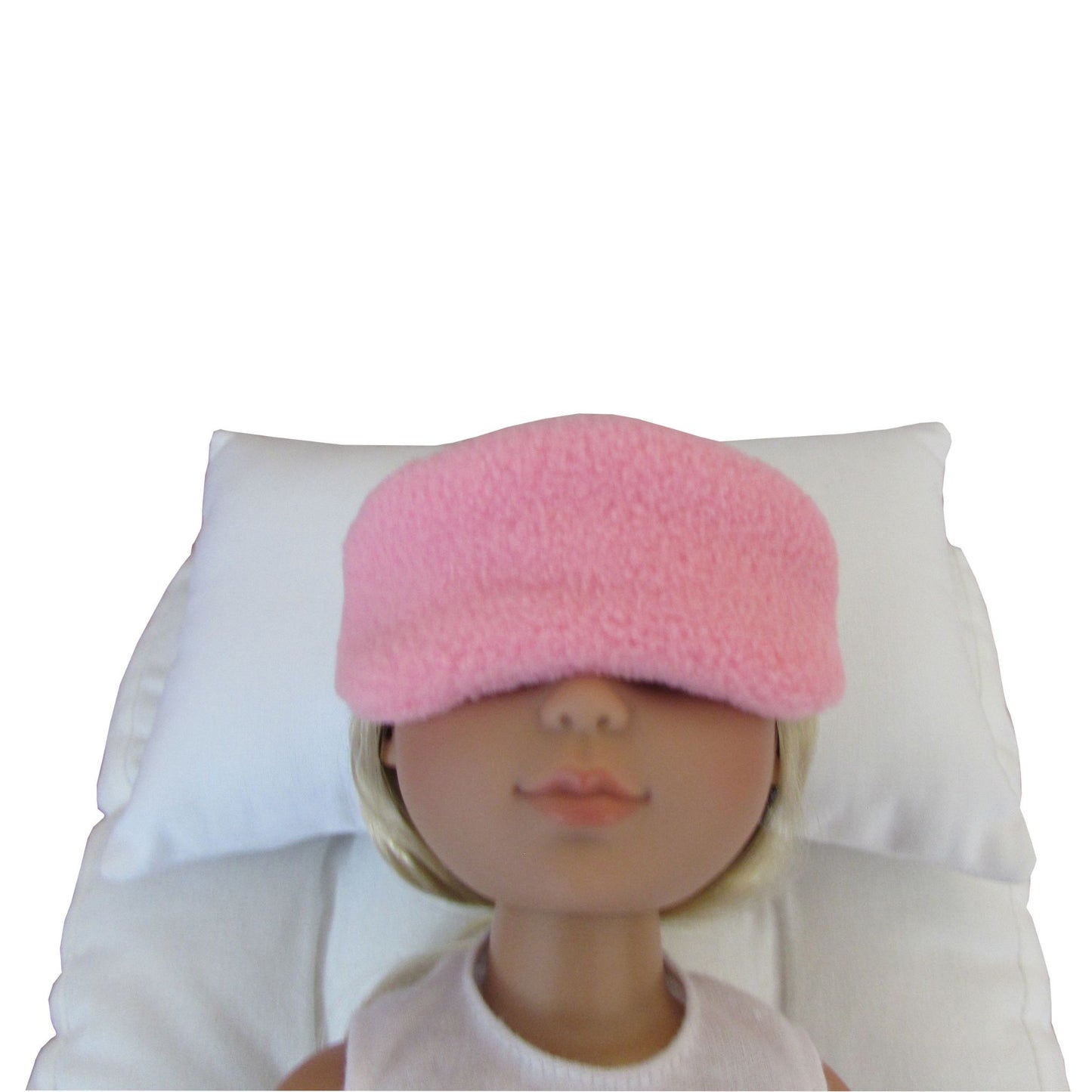 A pink fuzzy sleep mask worn by a doll lying on a white pillow against a white background.