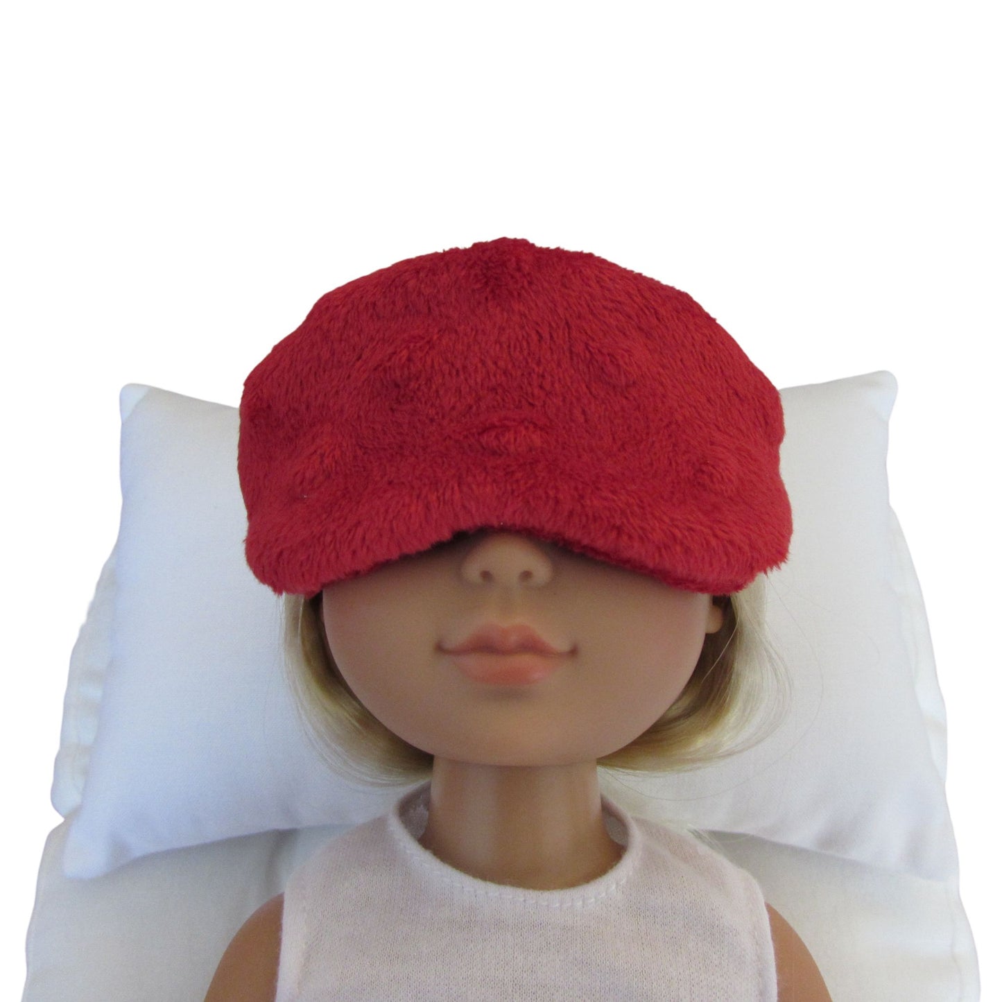 A red minky sleep mask shown on a doll's head resting against a white pillow, with the doll's face partially obscured by the mask.