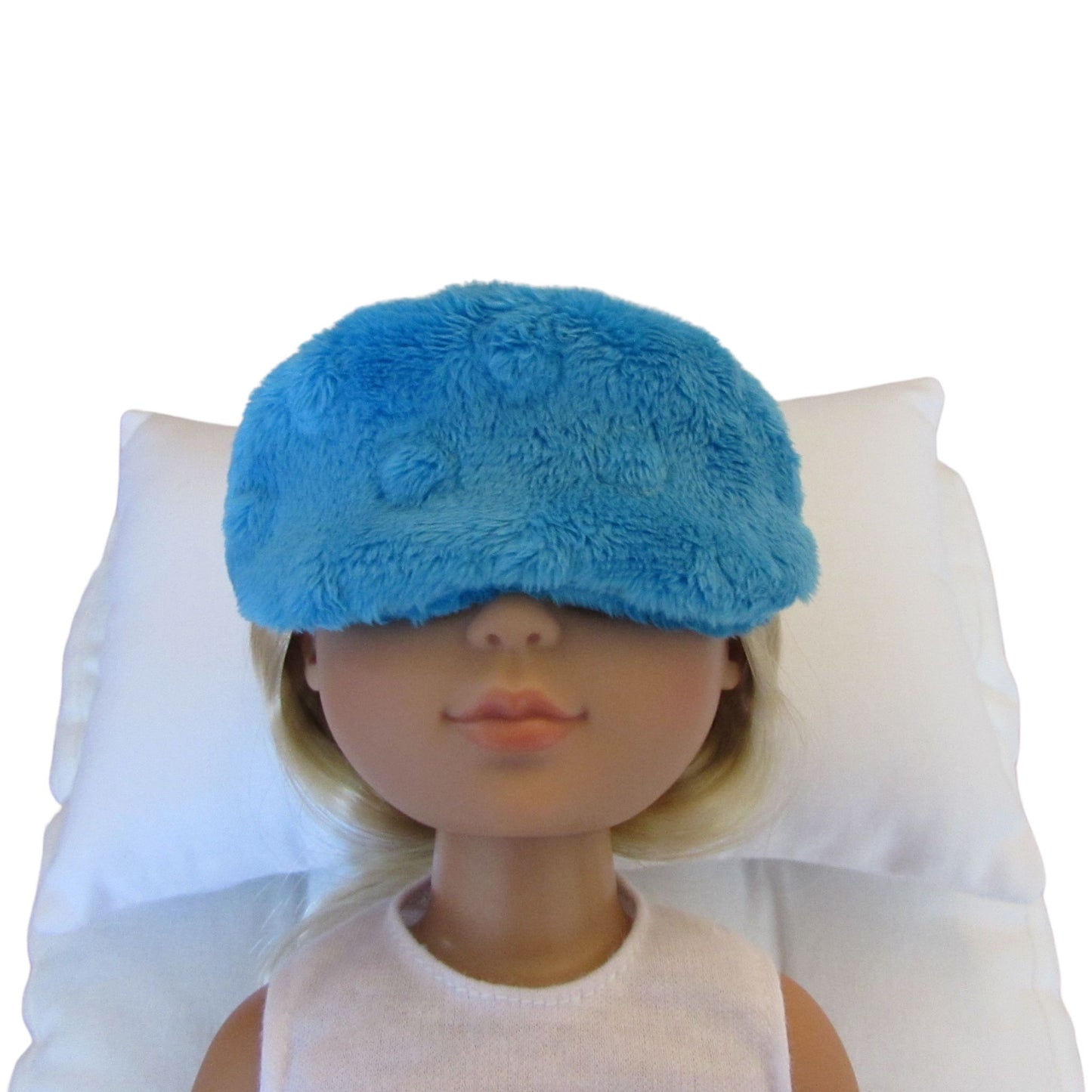 A turquoise minky sleep mask shown on a doll's face resting against a white pillow, photographed against a plain white background.