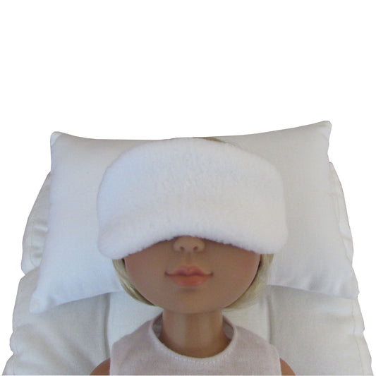 A white plush sleep mask worn by a doll, resting against a matching white pillow on a white background.