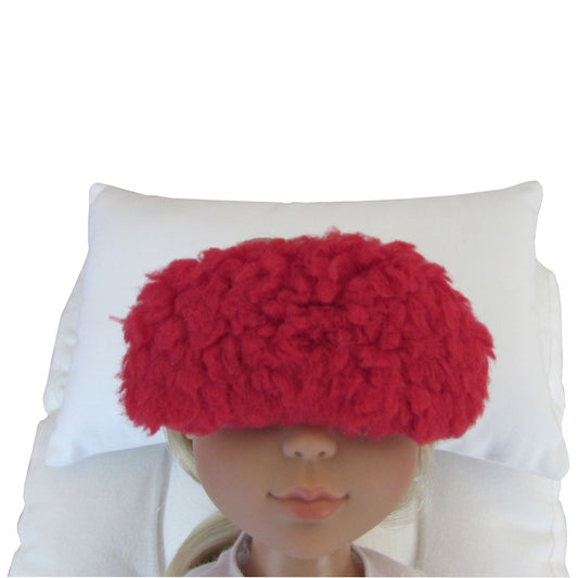 A bright red sleep mask displayed on a doll's face resting against a white pillow.