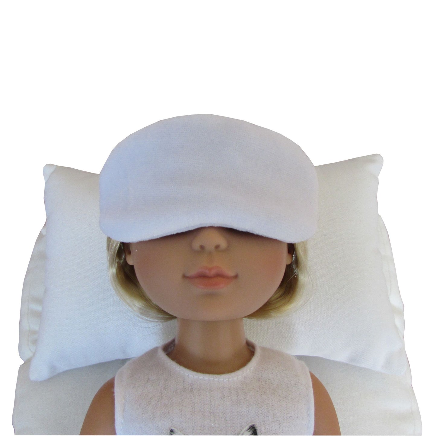 A doll with short blonde hair wearing a white stretch velvet sleep mask, resting on a white pillow against a white background.
