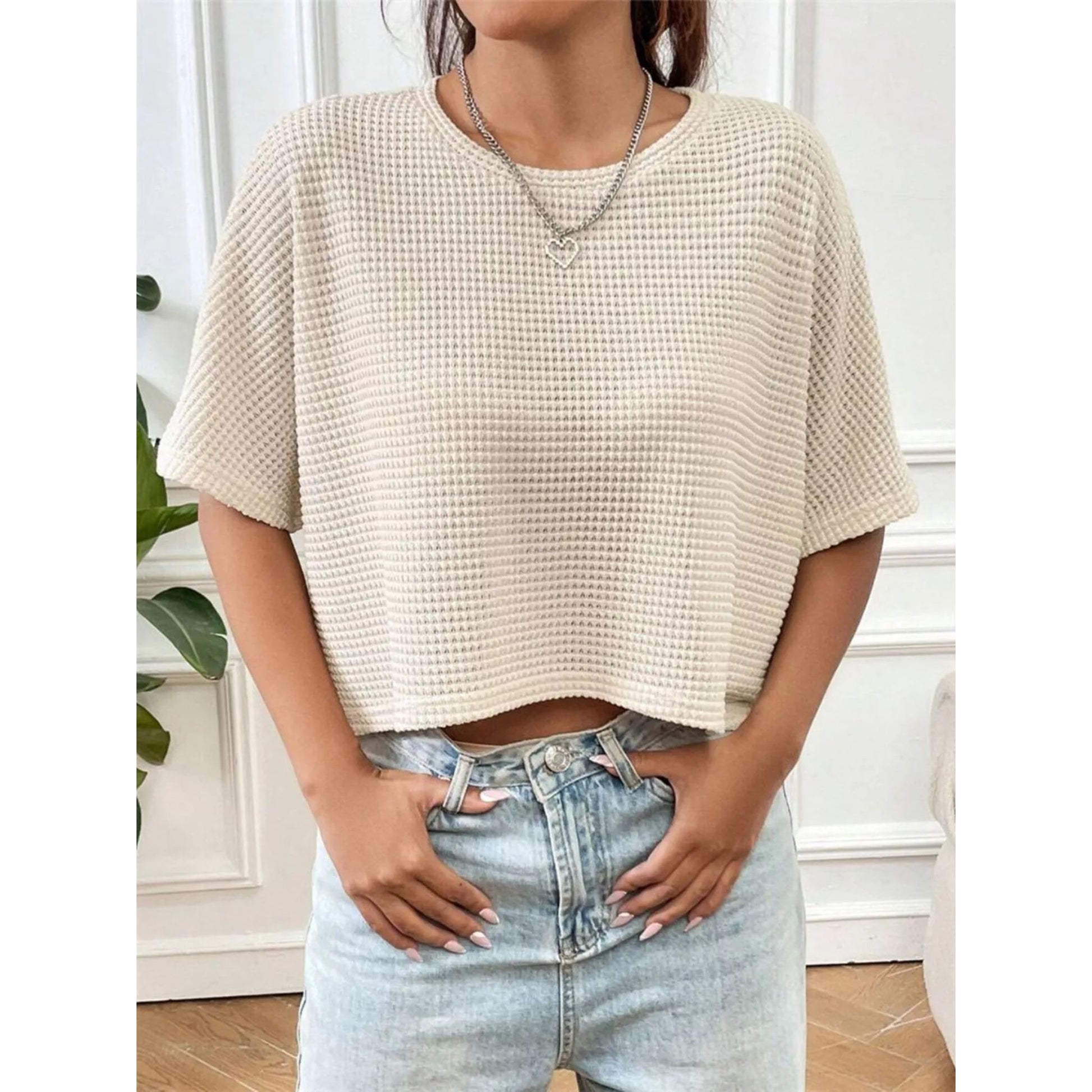 Person wearing a beige textured top and light blue jeans indoors.