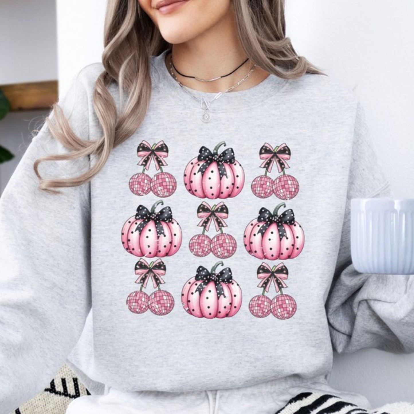 Person wearing a light gray sweatshirt with pink pumpkin designs and black bows.