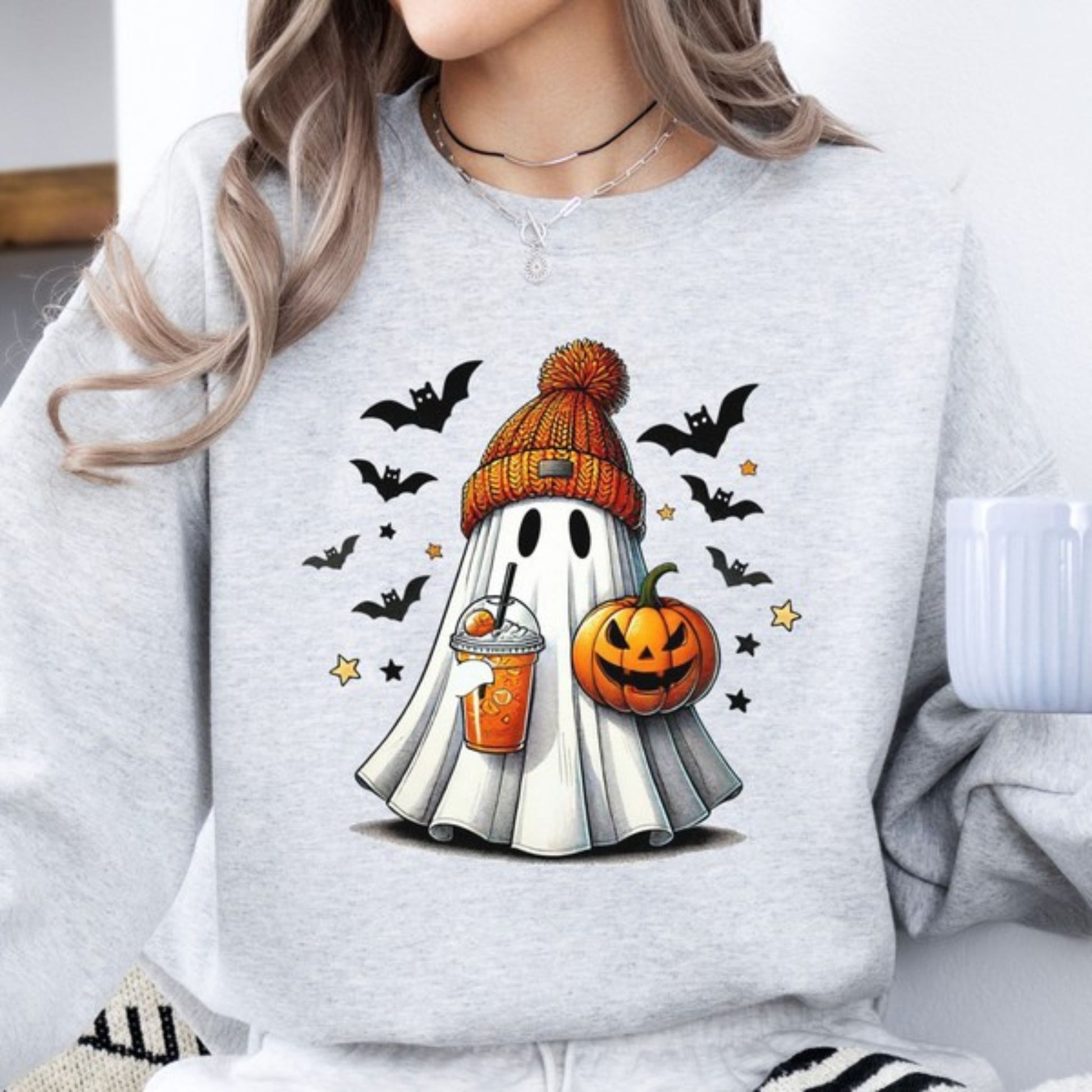 Person wearing a light gray sweatshirt with Halloween-themed ghost and pumpkin design.