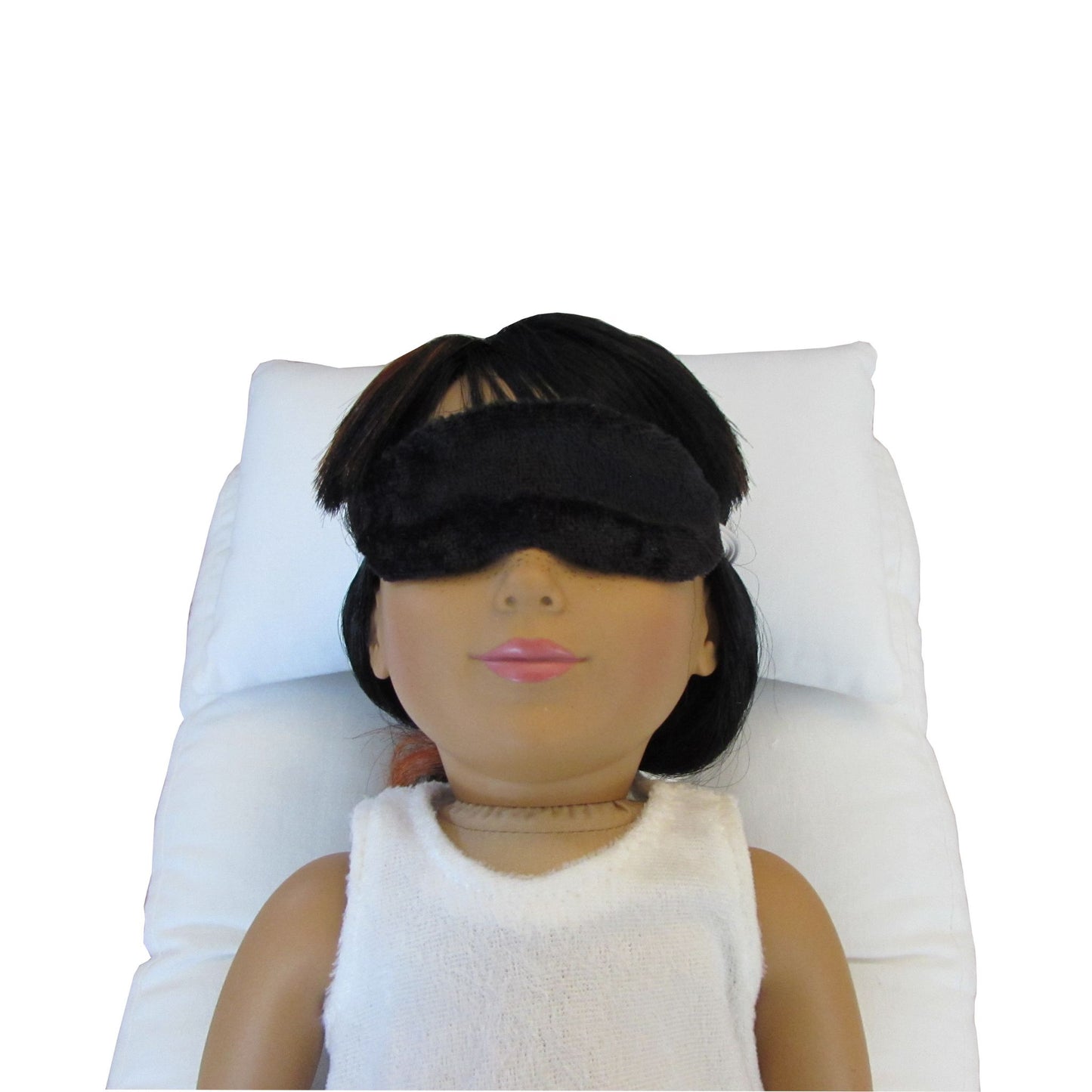 An 18-inch doll is wearing a black panne velvet sleep mask while lying on a white doll pillow and a white doll mattress.