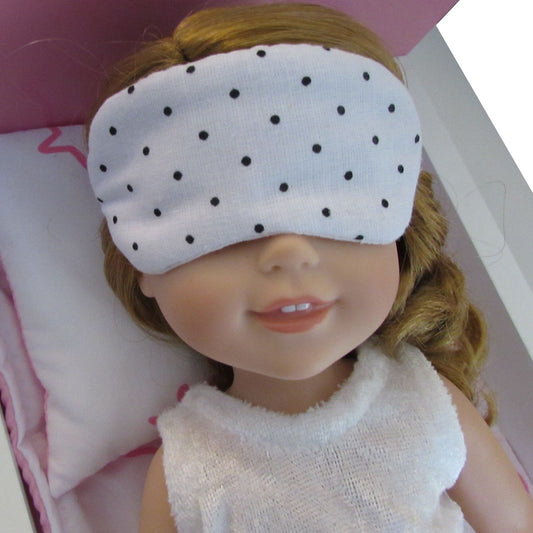 Doll wearing a white sleep mask with black polka dots on a pink pillow.