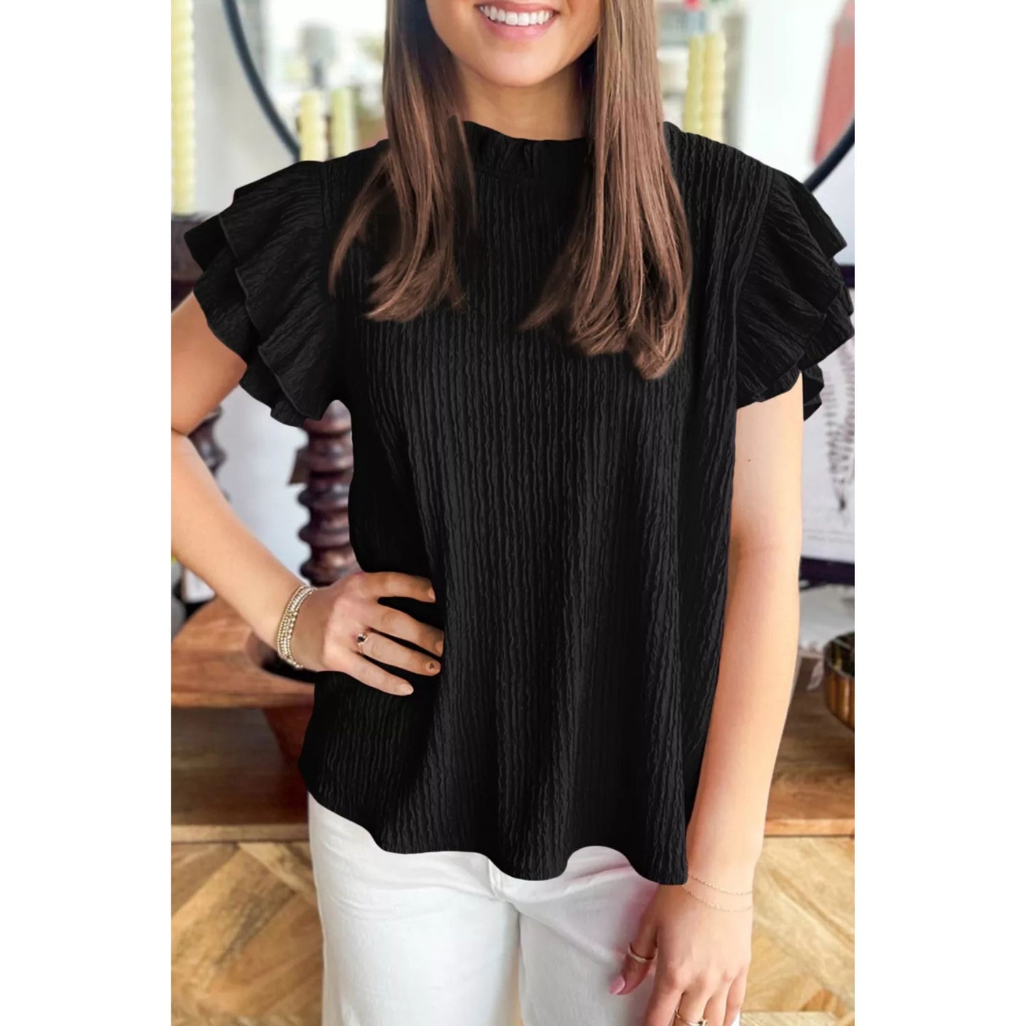 Woman wearing a black ruffled blouse with white pants in an indoor setting