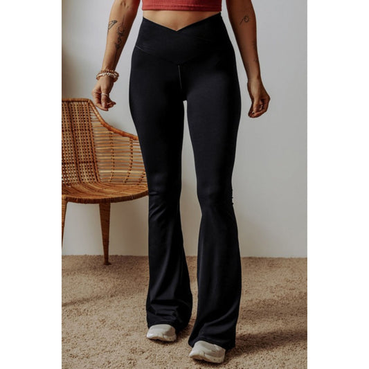 Person wearing black flared pants standing in a room with a wicker chair.