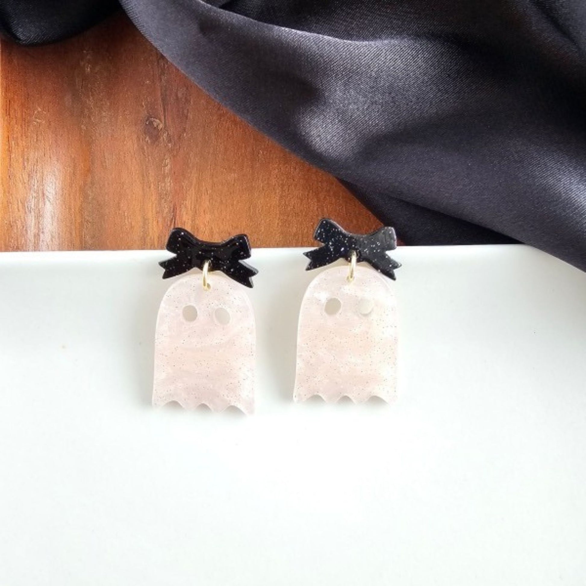 Ghost-shaped earrings with black bow details on a white surface.