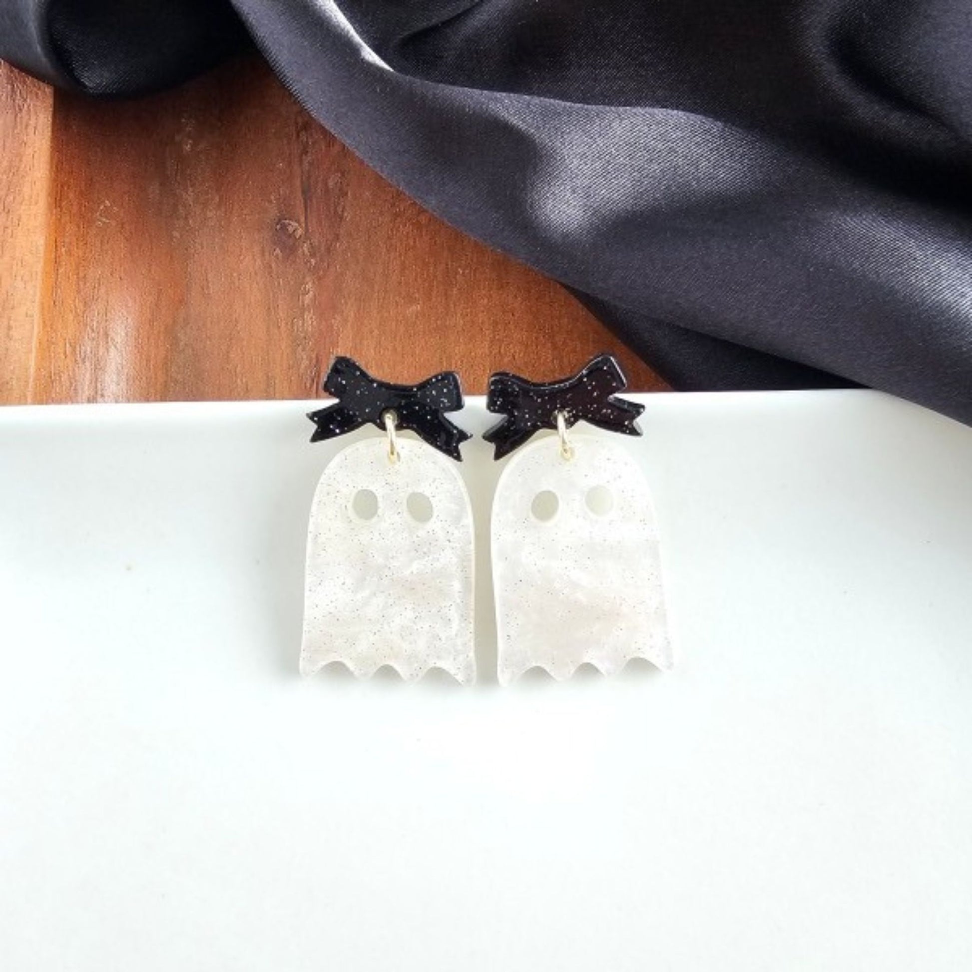 White ghost-shaped earrings with black bow accents on a white surface.
