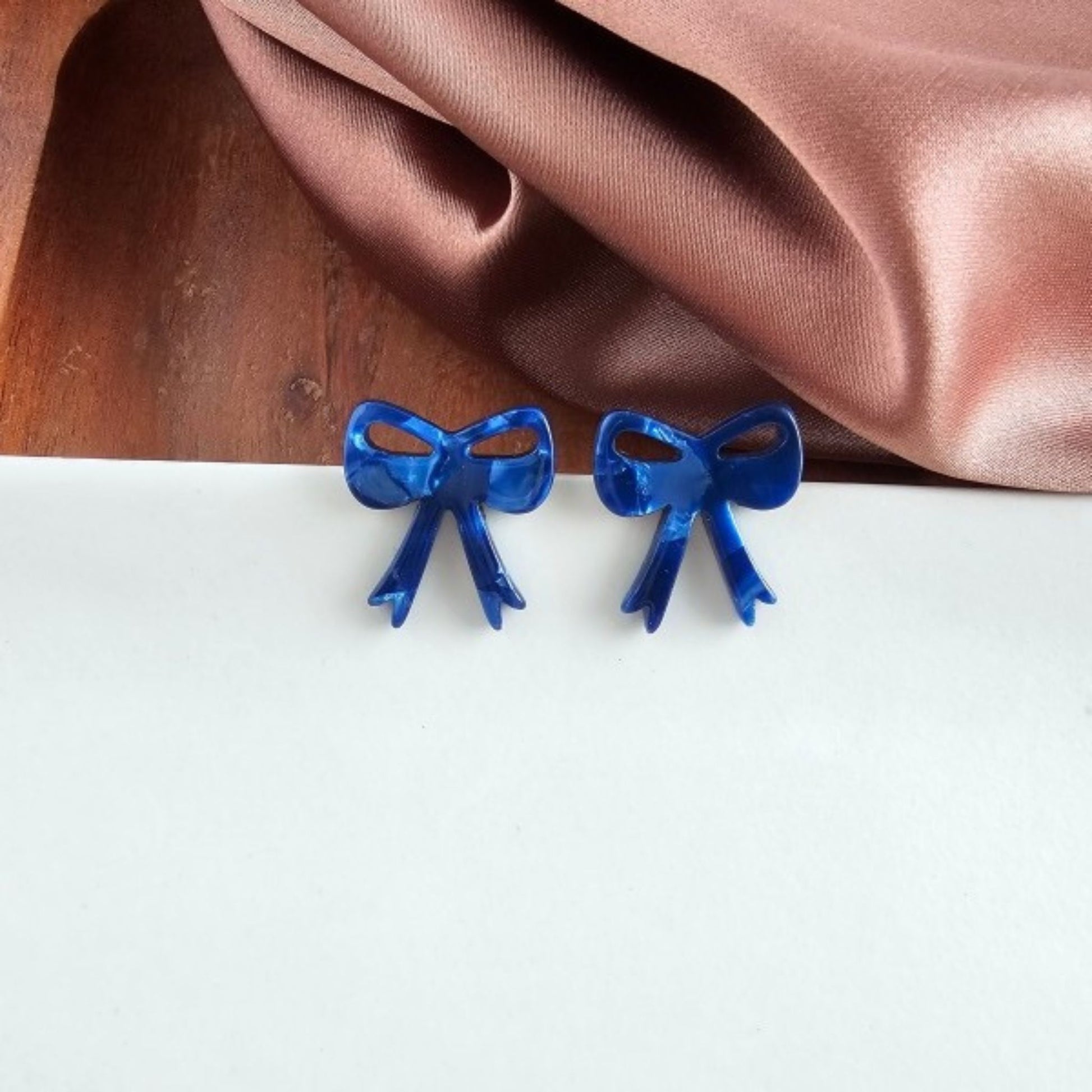 Blue bow-shaped earrings on a white surface with a brown fabric background