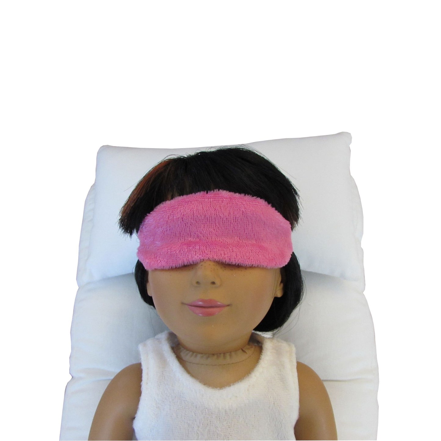 An 18-inch doll is wearing a bright pink panne velvet sleep mask while lying on a white doll pillow and a white doll mattress.