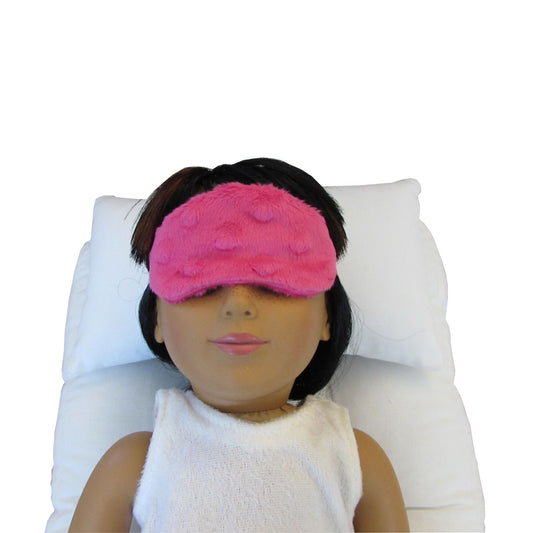 An 18-inch doll wearing a bright pink minky sleep mask while lying on a doll pillow and doll mattress.