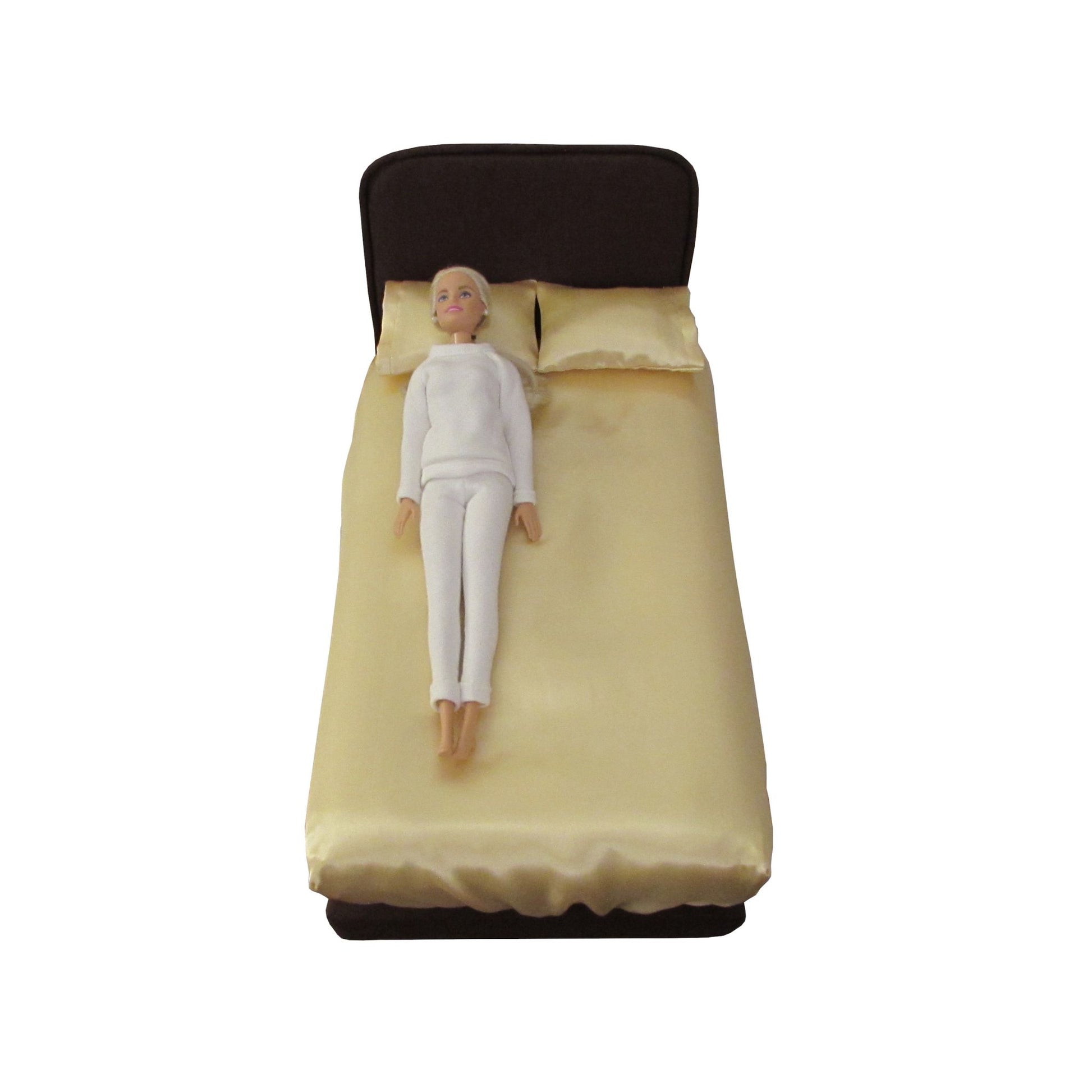 11.5-inch doll lying on a brown upholstered doll bed with light yellow pillowcases and fitted sheet