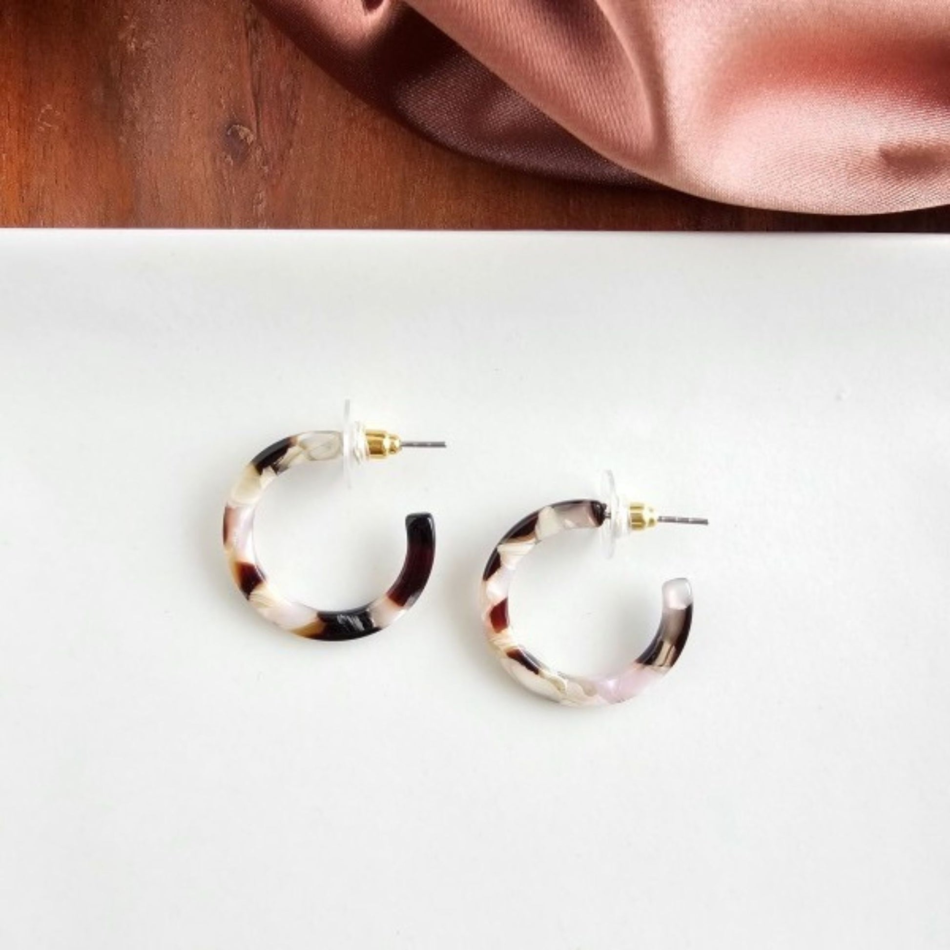 Tortoiseshell hoop earrings on a white surface with a pink fabric background