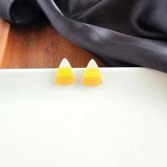 Candy corn-shaped earrings on a white surface with a dark fabric background