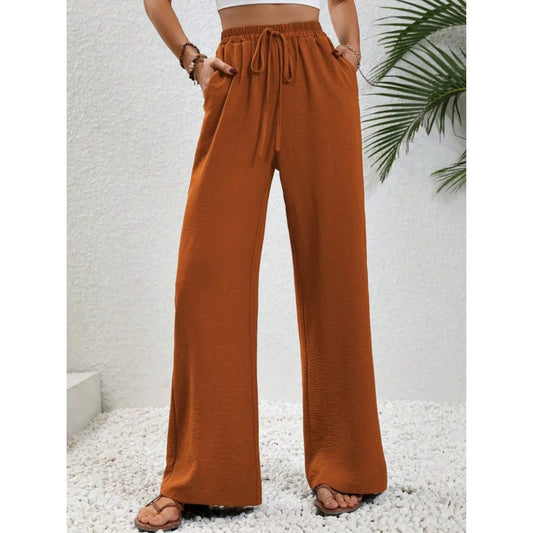 Person wearing rust-colored wide-leg pants with a white textured background