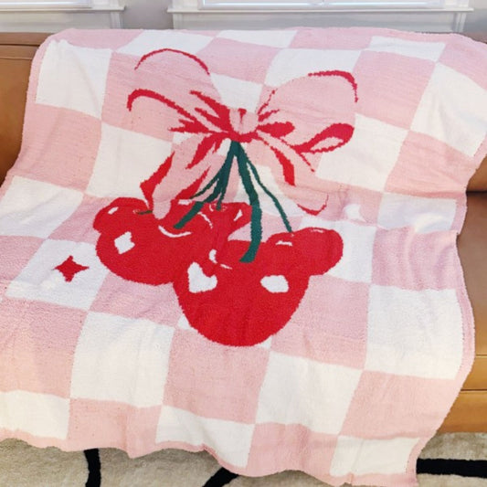 Pink checkered blanket with red cherries and a bow design on a wooden surface.