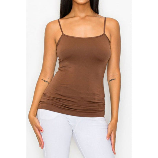 Woman wearing a brown spaghetti strap top and white pants on a plain background