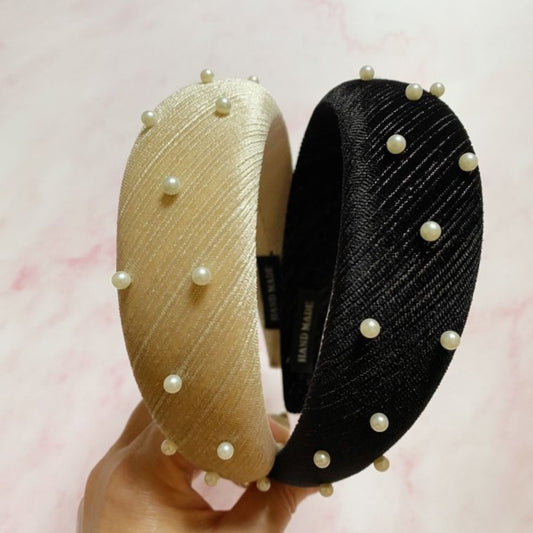 Two pearl-adorned headbands, one gold and one black, held against a pink background.