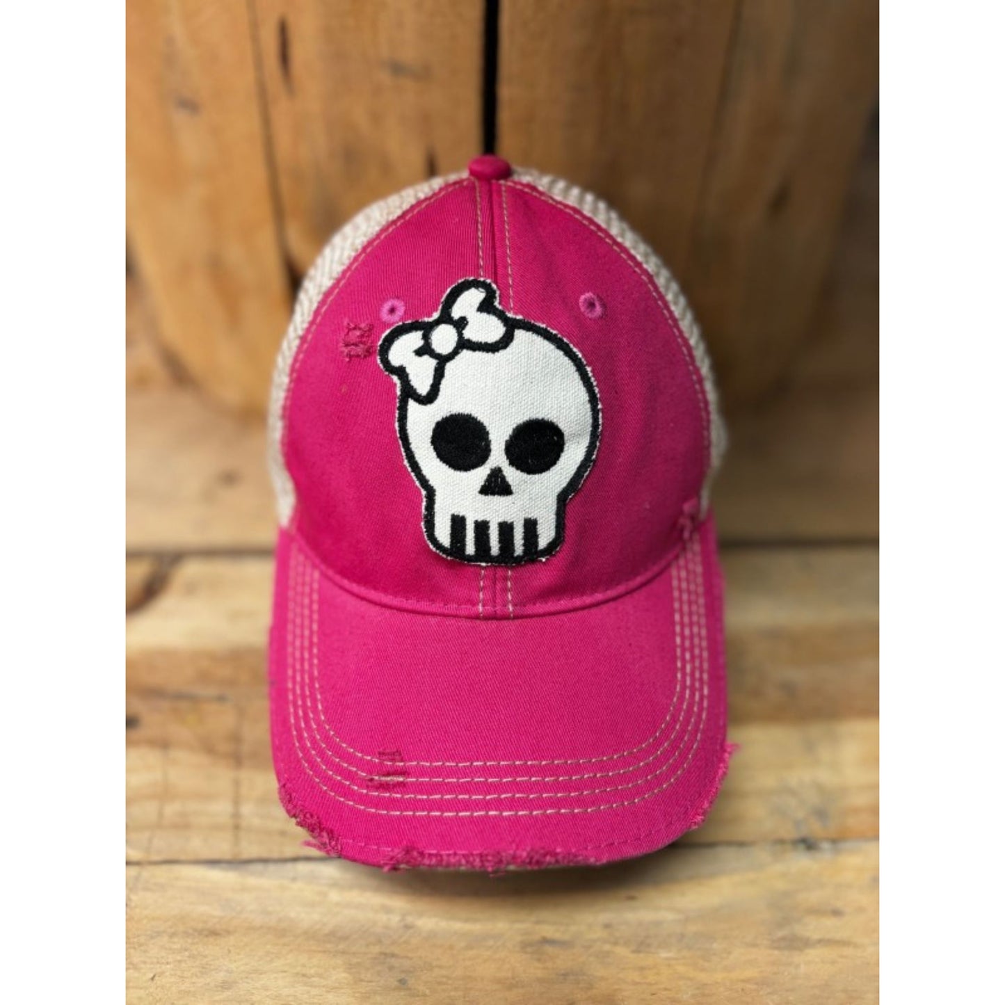 Pink cap with skull and bow design on a wooden surface