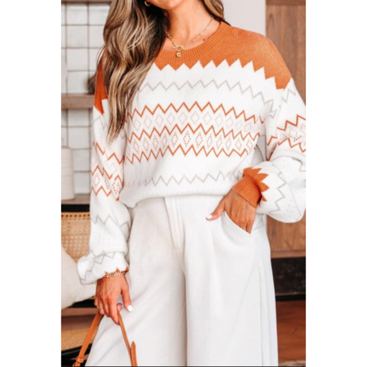 Person wearing a white sweater with orange geometric patterns and white pants indoors.