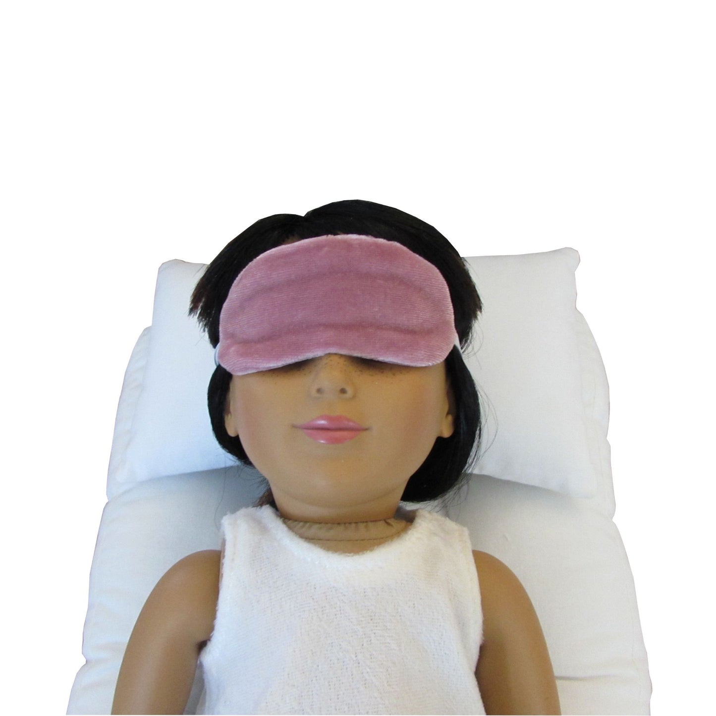 An 18-inch doll is wearing a dusty rose stretch velvet sleep mask while lying on a white doll pillow and a white doll mattress.