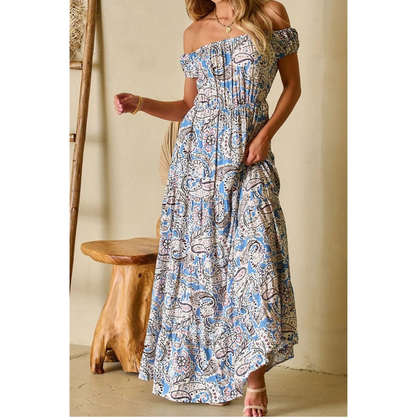 A woman is wearing a dusty blue boho paisley print off the shoulder maxi dress.