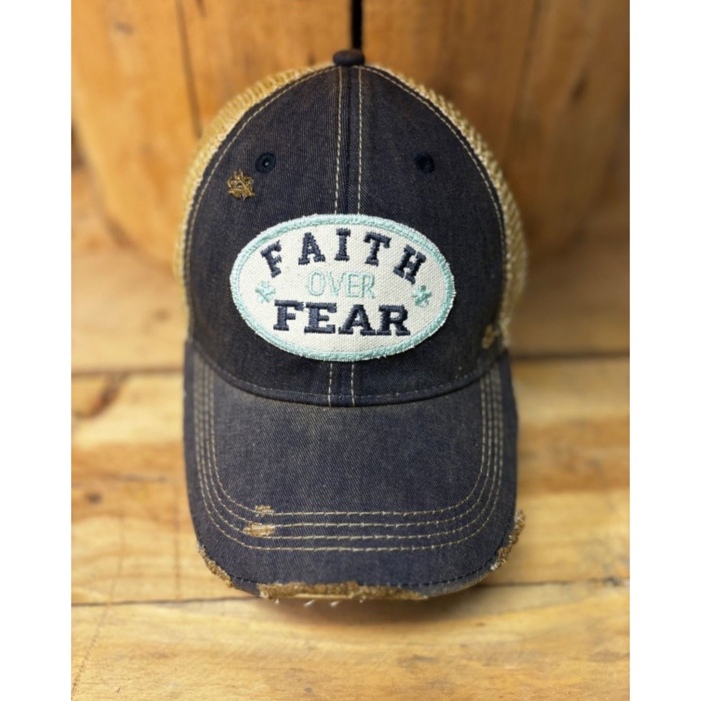 Black distressed cap with 'Faith Over Fear' patch on a wooden surface