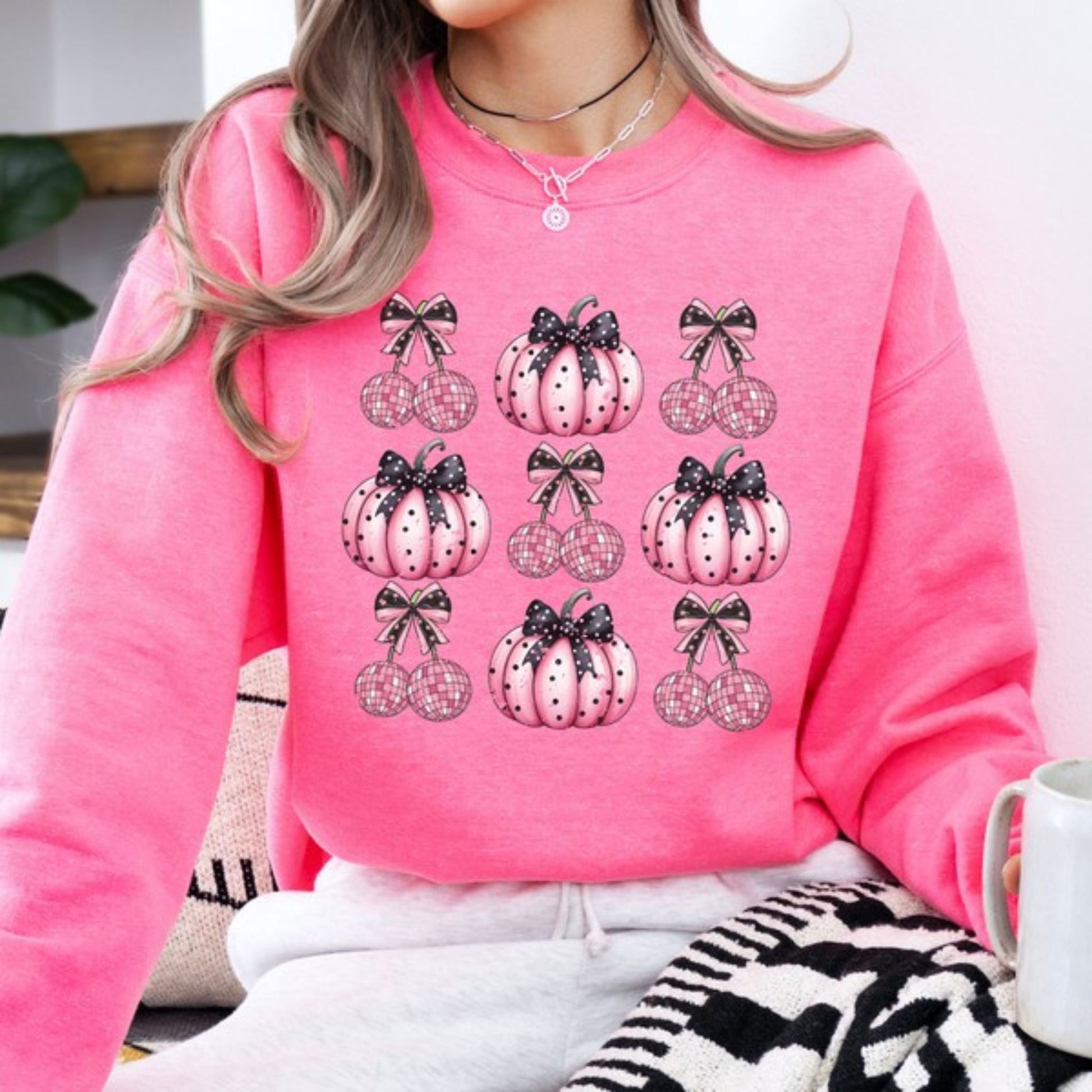 Person wearing a pink sweatshirt with pumpkin and bow designs, sitting indoors.
