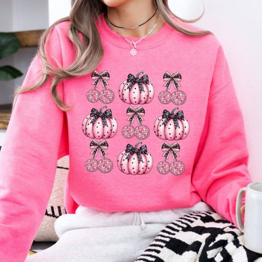 Person wearing a pink sweatshirt with pumpkin and bow designs, sitting indoors.