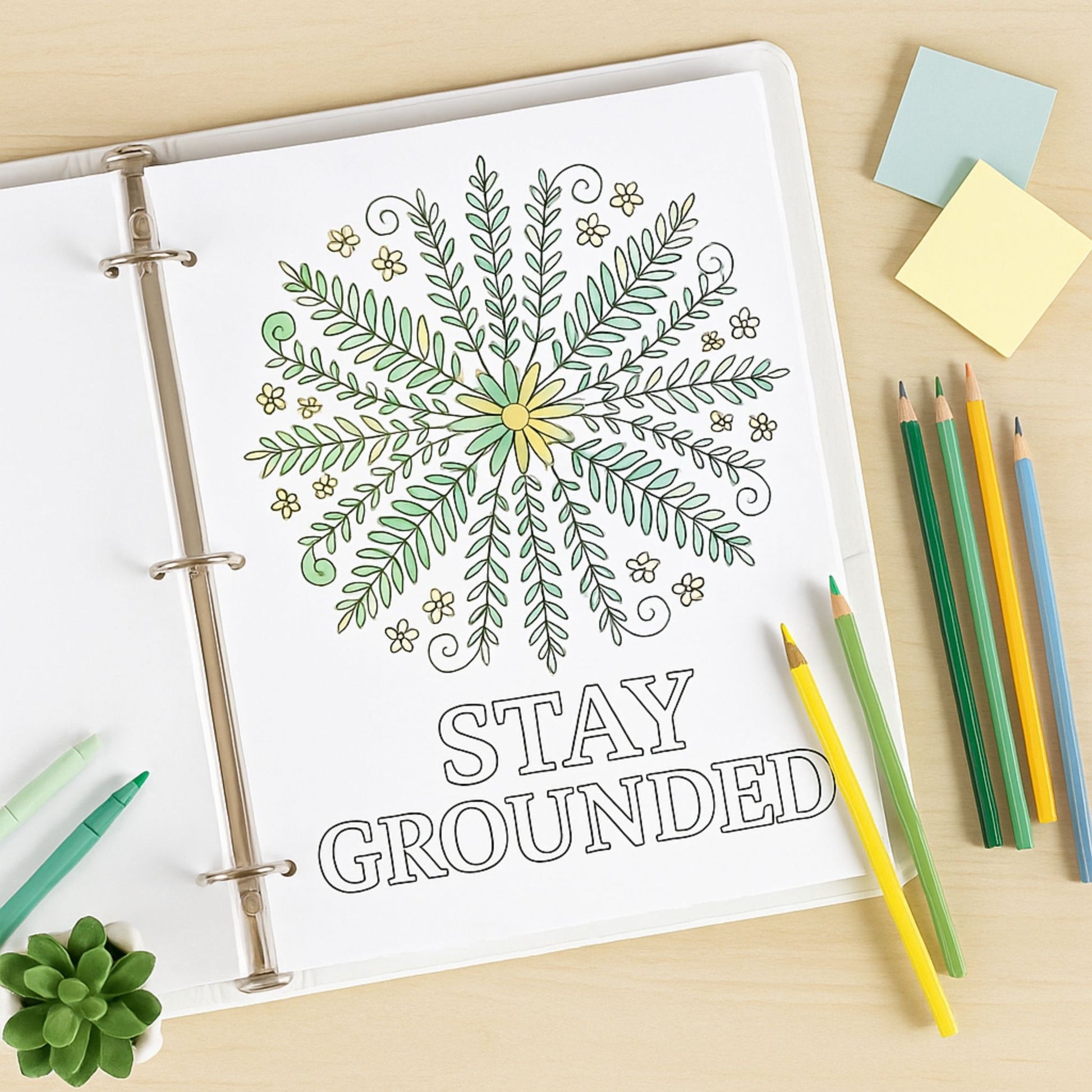 Coloring book page with a leafy design and 'Stay Grounded' text, surrounded by colored pencils and sticky notes.