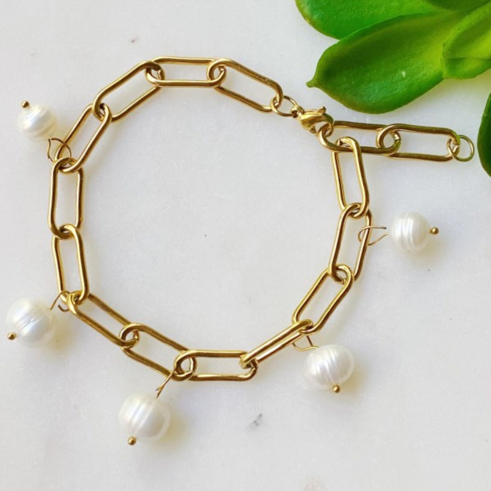 Gold chain bracelet with pearls on a white surface with green leaves.