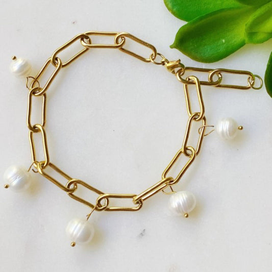 Gold chain bracelet with pearls on a white surface with green leaves.