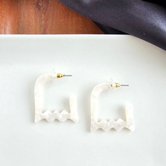 White hoop earrings on a white surface with a wooden and fabric background