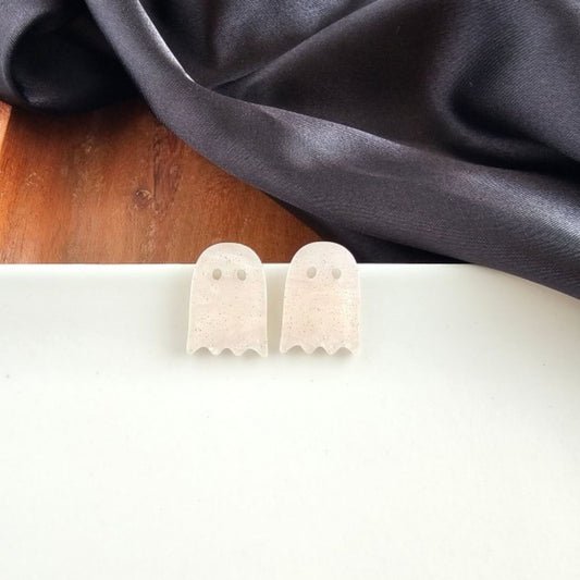 Ghost-shaped earrings on a white surface with a dark fabric background