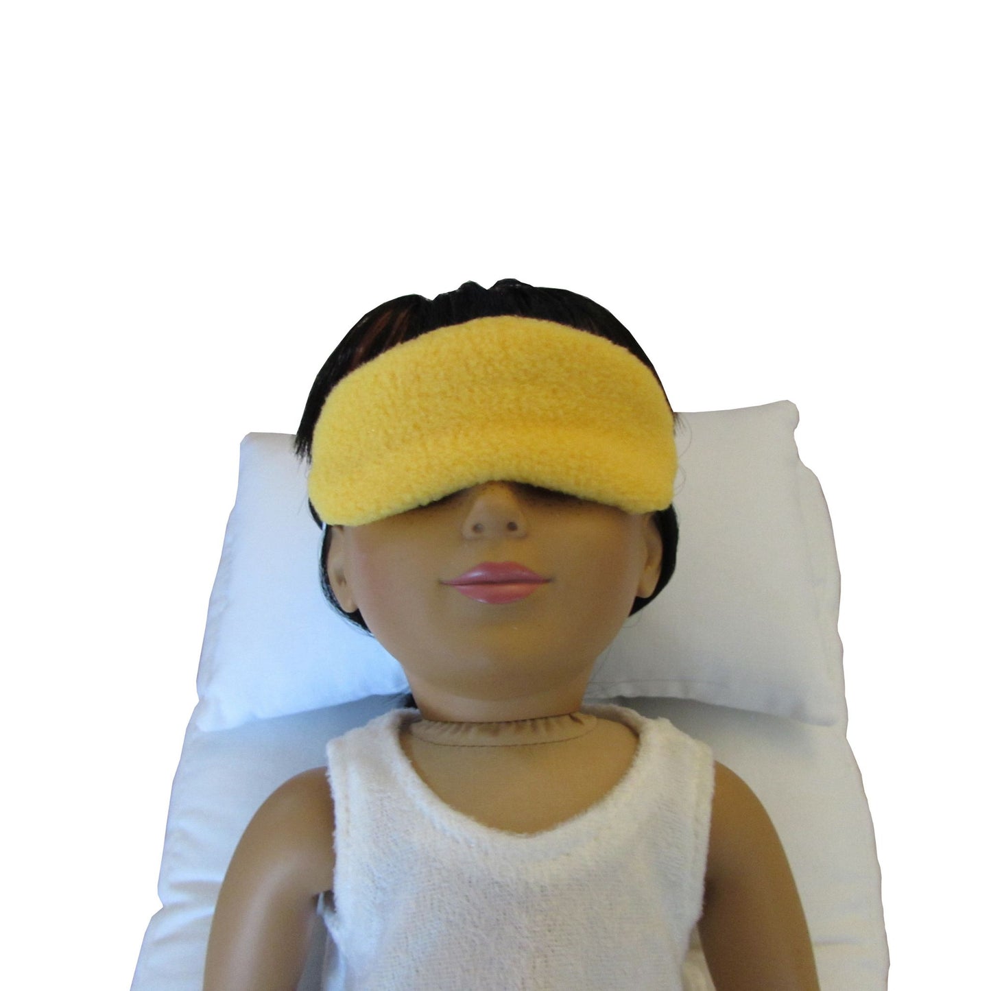 An 18-inch doll wearing a gold anti-pill fleece sleep mask while wearing a white doll pillow and a white doll mattress.