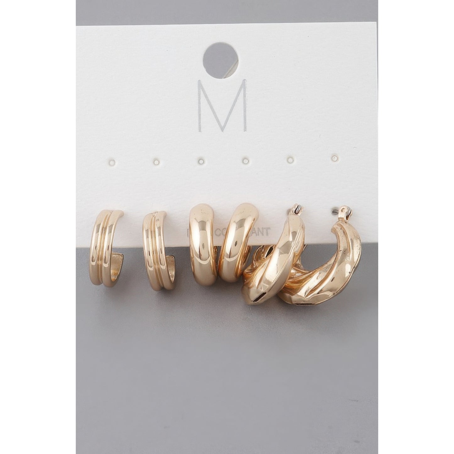 A set of three gold-toned hoop earrings displayed on a white jewelry card with a gray background.