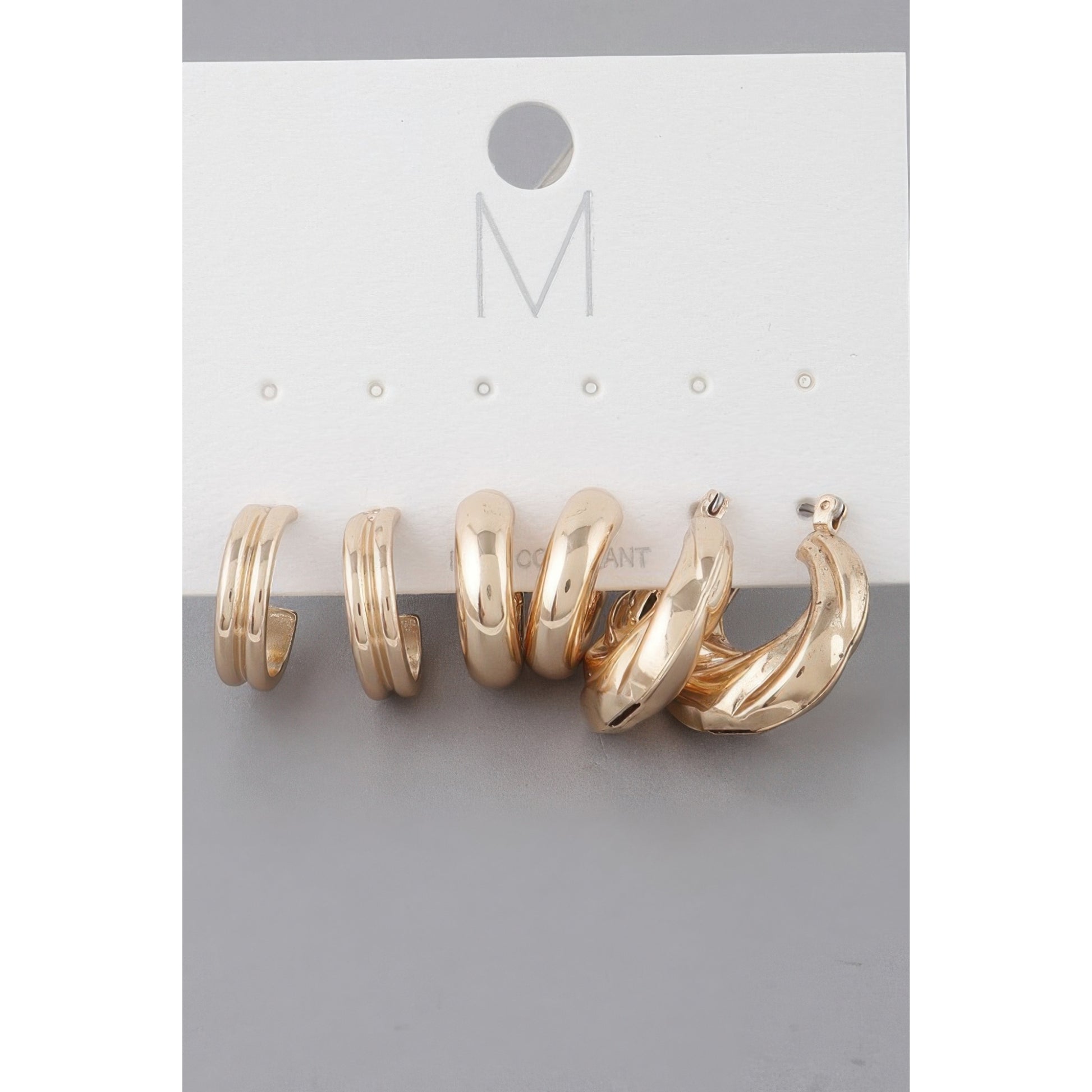 A set of three gold-toned hoop earrings displayed on a white jewelry card with a gray background.