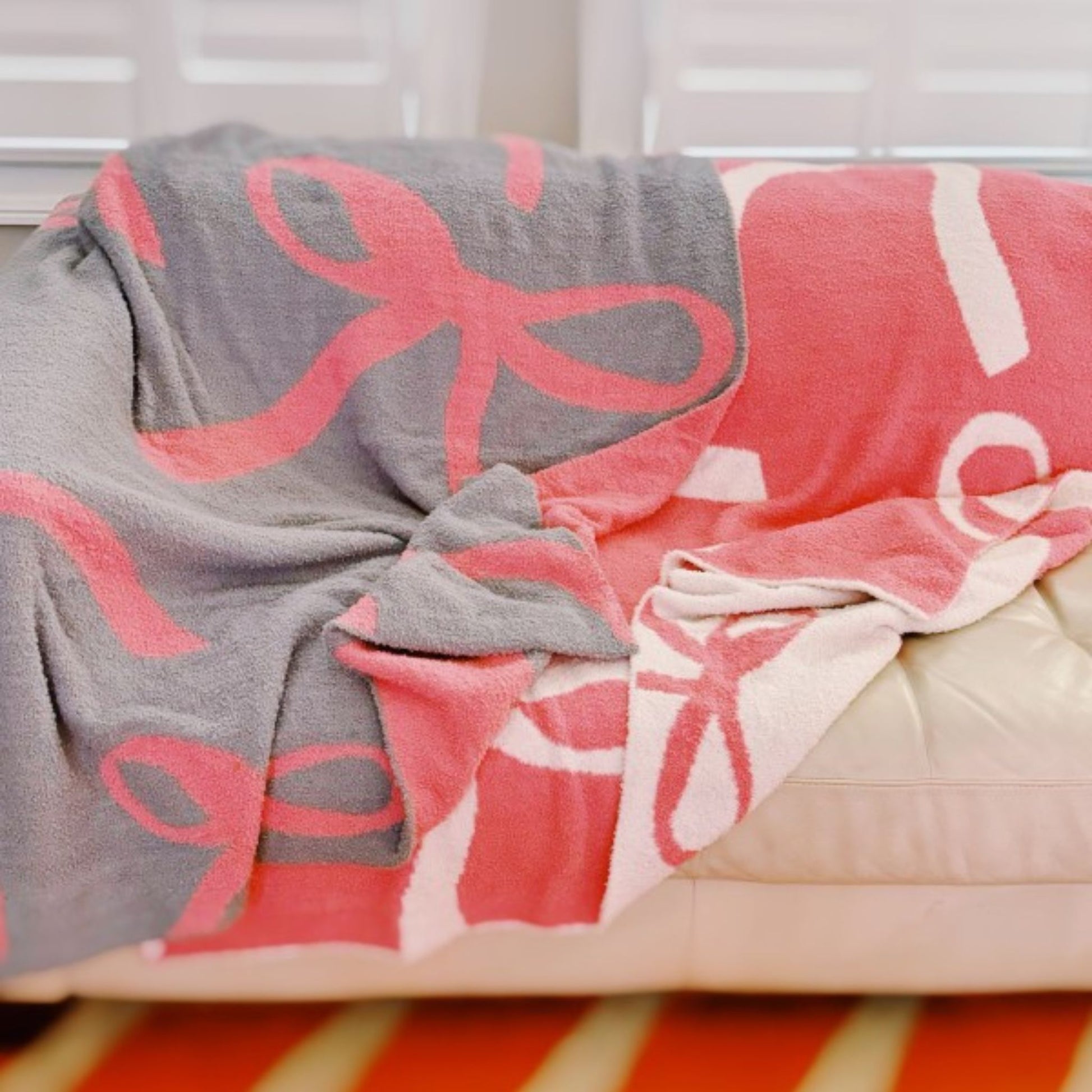 Gray and pink blanket with bow pattern draped over a bed.